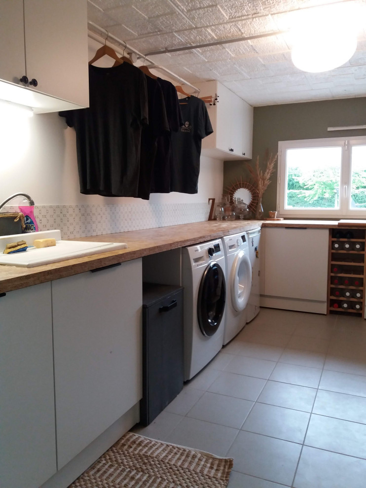 Exempel på en mellanstor skandinavisk l-formad tvättstuga enbart för tvätt, med en undermonterad diskho, träbänkskiva, grönt stänkskydd, gröna väggar, en tvättmaskin och torktumlare bredvid varandra och grått golv
