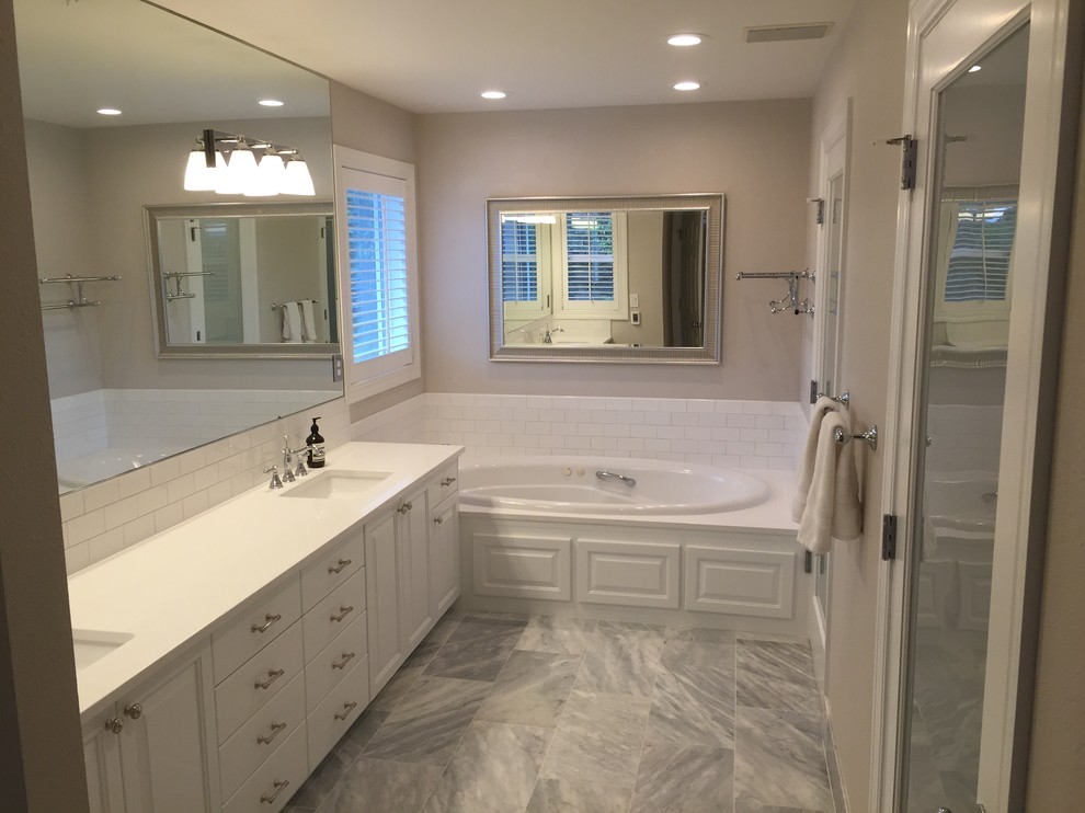 This is an example of a mid-sized transitional master bathroom in Portland with raised-panel cabinets, white cabinets, a drop-in tub, white tile, subway tile, grey walls, marble floors, an undermount sink and solid surface benchtops.