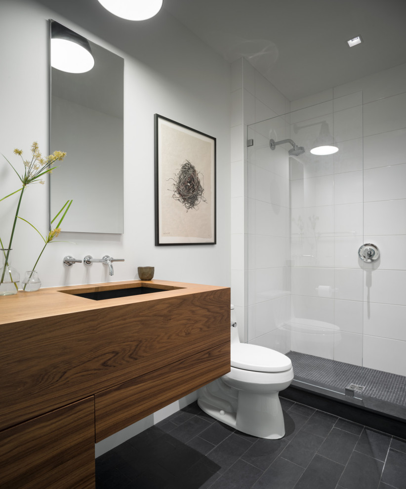 Modern master wet room bathroom in Portland Maine with flat-panel cabinets, dark wood cabinets, a one-piece toilet, slate floors, an undermount sink, wood benchtops, black floor, a hinged shower door, white benchtops, a double vanity and a floating vanity.