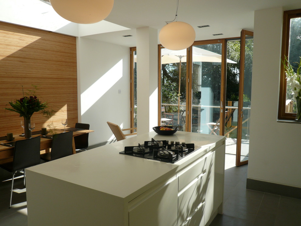 This is an example of a mid-sized modern galley open plan kitchen in Manchester with flat-panel cabinets, white cabinets, solid surface benchtops, green splashback, glass sheet splashback and multiple islands.
