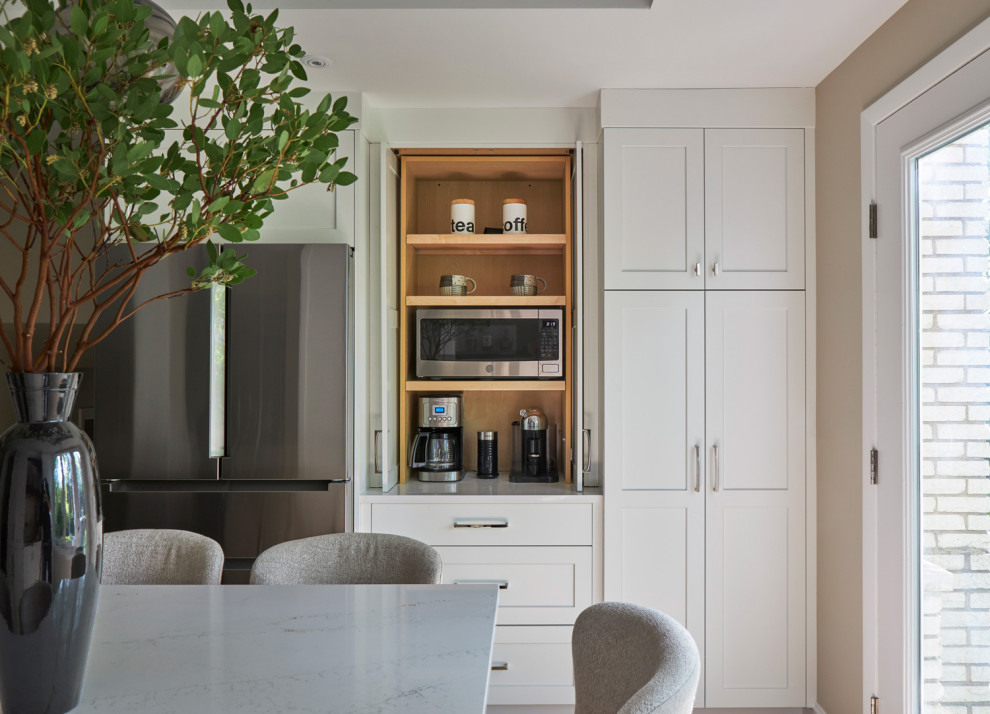 Example of a large transitional u-shaped light wood floor, brown floor and coffered ceiling eat-in kitchen design in Chicago with a farmhouse sink, shaker cabinets, white cabinets, quartz countertops, white backsplash, subway tile backsplash, stainless steel appliances, an island and multicolored countertops