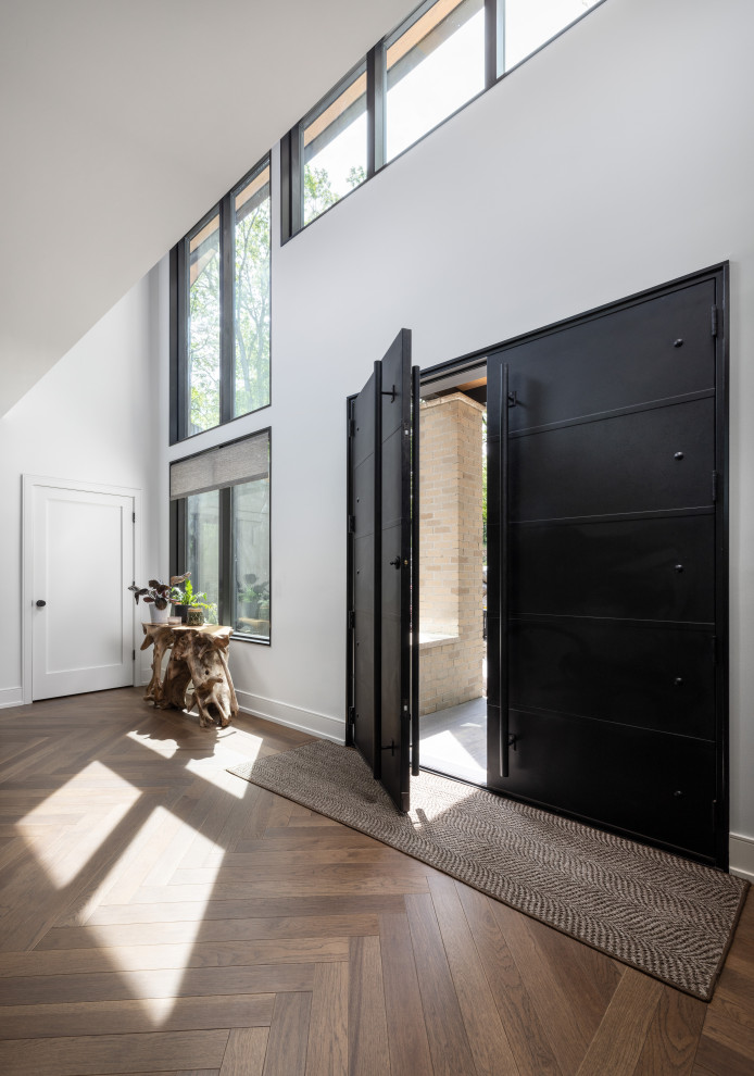 На фото: большая входная дверь в стиле неоклассика (современная классика) с белыми стенами, темным паркетным полом, двустворчатой входной дверью, металлической входной дверью и коричневым полом с