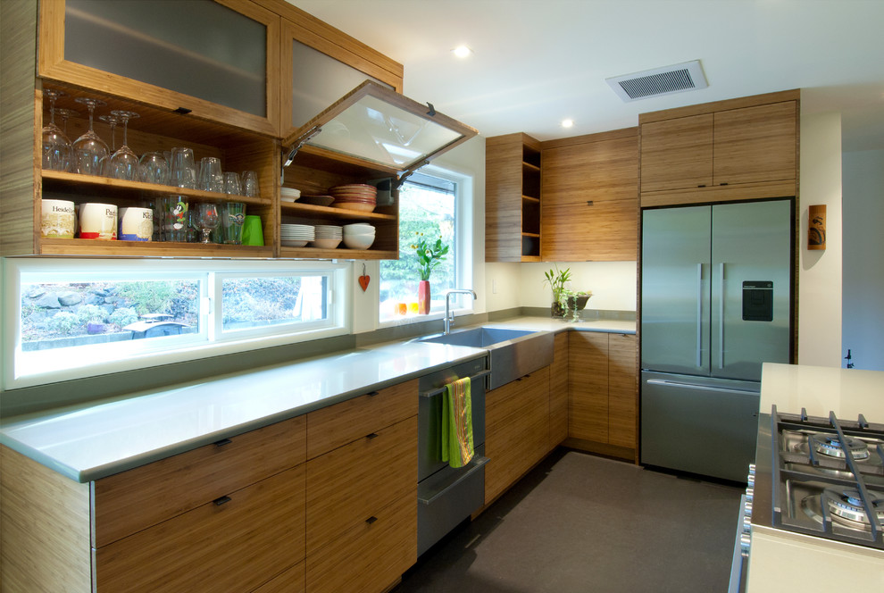 Photo of a small midcentury kitchen in Seattle with a farmhouse sink, glass-front cabinets, light wood cabinets, quartz benchtops, stainless steel appliances and grey benchtop.