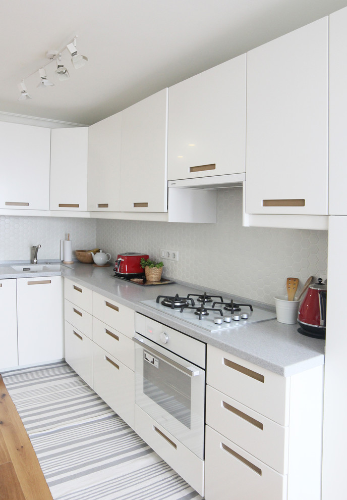 Inspiration for a mid-sized contemporary l-shaped kitchen in Moscow with an undermount sink, flat-panel cabinets, white cabinets, solid surface benchtops, white splashback, mosaic tile splashback, white appliances, medium hardwood floors and no island.