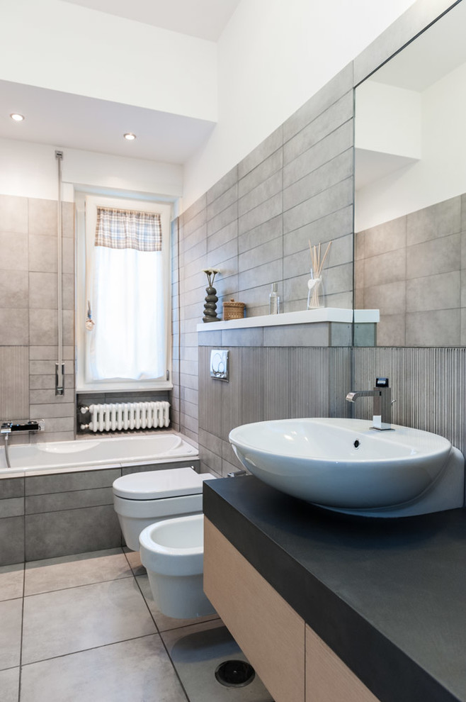 Photo of a contemporary master bathroom in Rome with flat-panel cabinets, light wood cabinets, a drop-in tub, a wall-mount toilet, ceramic tile and a vessel sink.