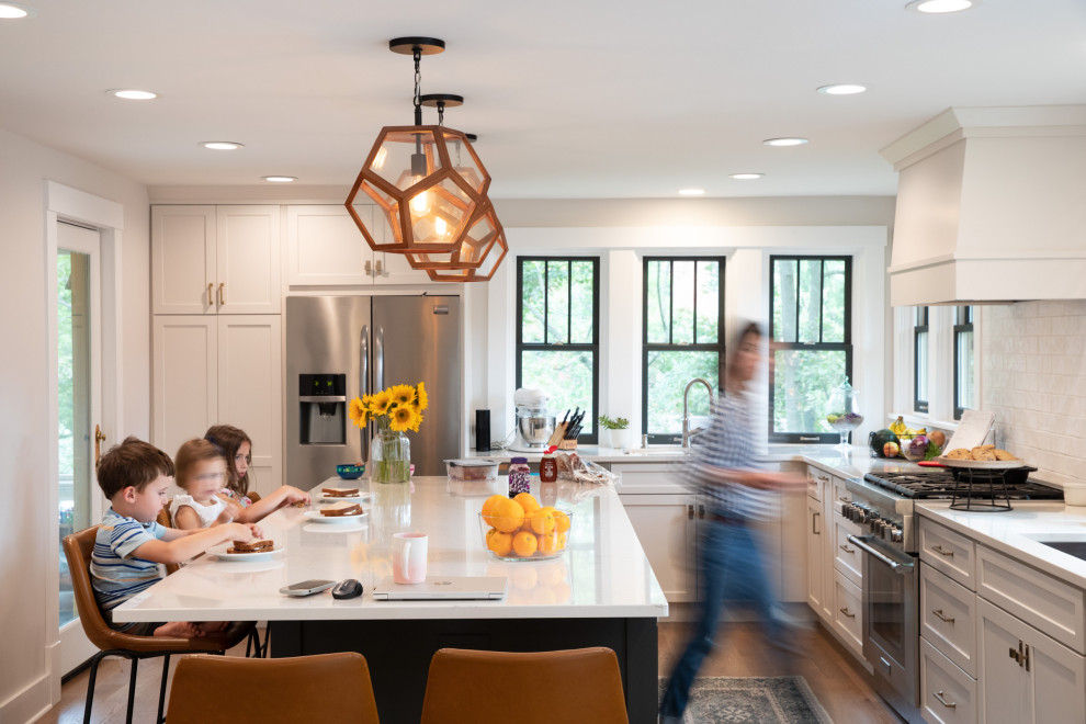 Transitional l-shaped medium tone wood floor and brown floor eat-in kitchen photo with a drop-in sink, shaker cabinets, white cabinets, quartzite countertops, white backsplash, subway tile backsplash, stainless steel appliances, an island and white countertops
