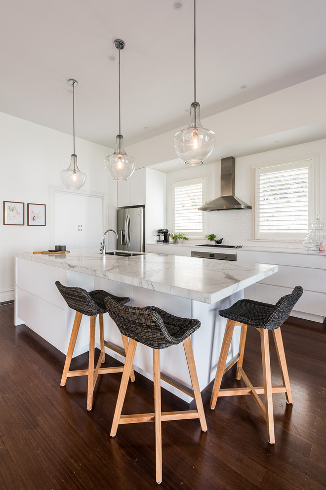 Mid-sized contemporary single-wall kitchen in Melbourne with an undermount sink, flat-panel cabinets, white cabinets, marble benchtops, white splashback, subway tile splashback, stainless steel appliances, dark hardwood floors, with island and brown floor.