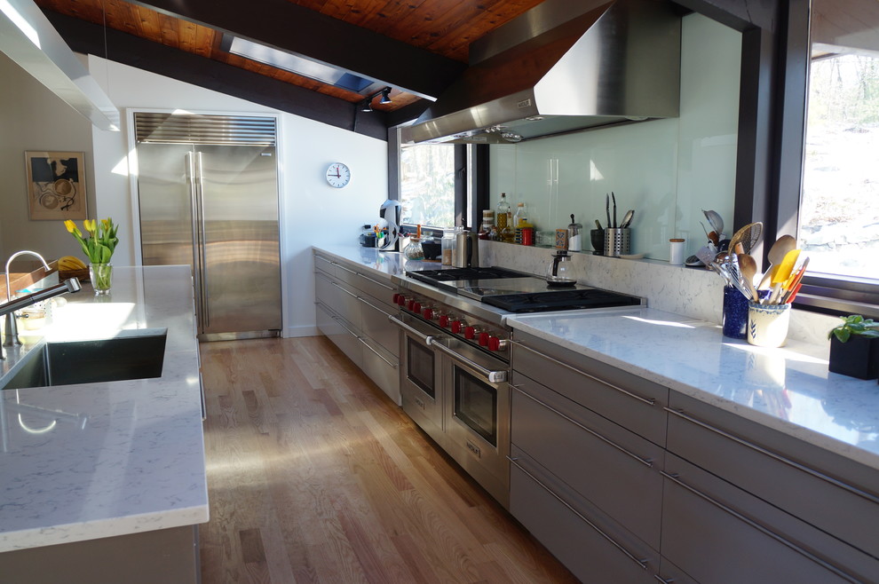 Inspiration for a mid-sized contemporary galley eat-in kitchen in Boston with flat-panel cabinets, grey cabinets, solid surface benchtops, green splashback, glass tile splashback, stainless steel appliances, with island, a single-bowl sink, light hardwood floors, brown floor and white benchtop.