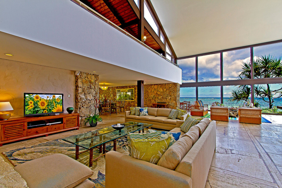 Inspiration for an expansive tropical open concept family room in Hawaii with white walls, a standard fireplace, a stone fireplace surround, no tv and beige floor.