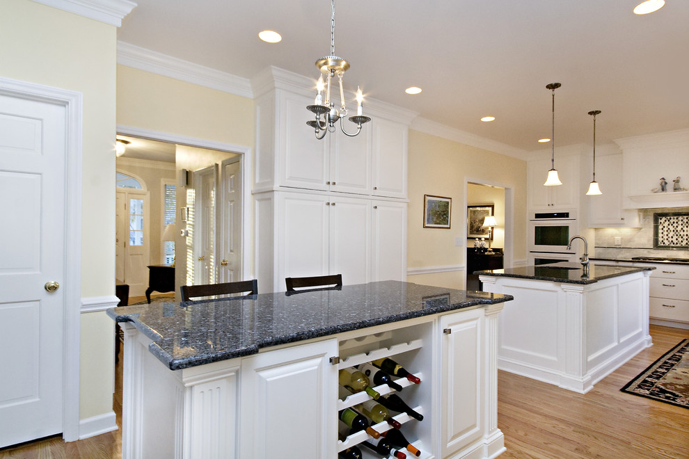 Inspiration for a large traditional l-shaped eat-in kitchen in Raleigh with an undermount sink, raised-panel cabinets, white cabinets, granite benchtops, white splashback, subway tile splashback, white appliances, blue benchtop and multiple islands.