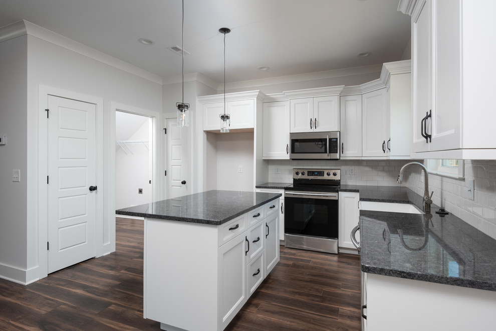 Open concept kitchen - mid-sized transitional l-shaped dark wood floor and brown floor open concept kitchen idea with a farmhouse sink, shaker cabinets, white cabinets, granite countertops, white backsplash, subway tile backsplash, stainless steel appliances, an island and black countertops