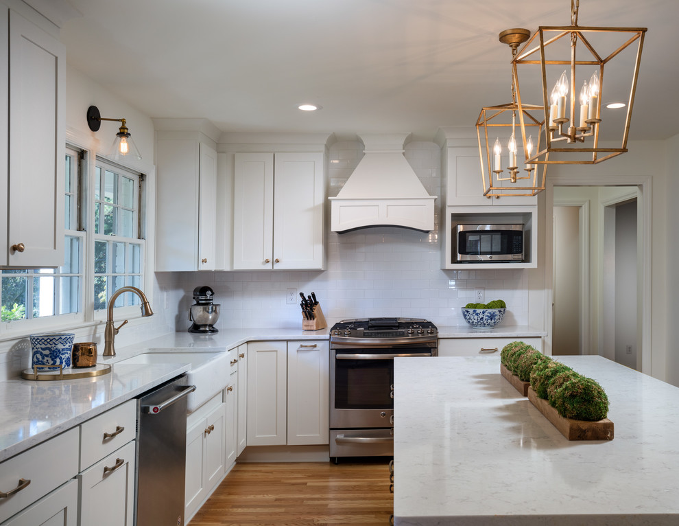 Design ideas for a large transitional l-shaped eat-in kitchen in Atlanta with a farmhouse sink, recessed-panel cabinets, white cabinets, quartz benchtops, white splashback, subway tile splashback, stainless steel appliances, medium hardwood floors, with island and brown floor.