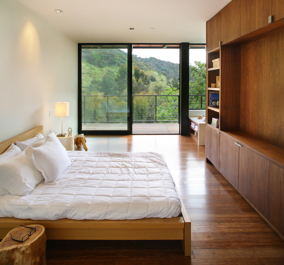 This is an example of a modern bedroom in Los Angeles with white walls, dark hardwood floors and no fireplace.