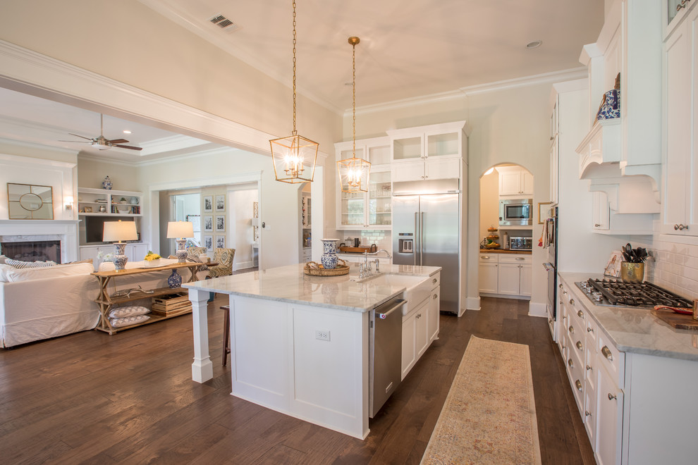 Design ideas for a large traditional l-shaped open plan kitchen in Houston with a farmhouse sink, shaker cabinets, white cabinets, quartzite benchtops, white splashback, subway tile splashback, stainless steel appliances, dark hardwood floors, with island, brown floor and white benchtop.