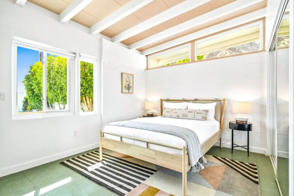 Midcentury guest bedroom in Other with white walls, laminate floors, green floor, exposed beam and brick walls.