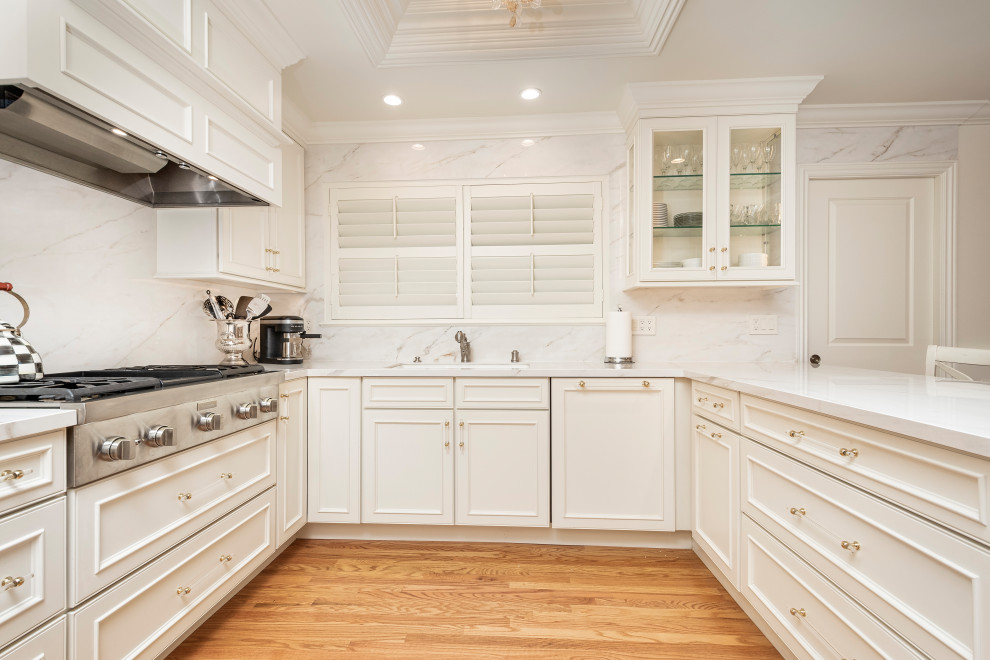 Mid-sized elegant u-shaped medium tone wood floor, brown floor and tray ceiling eat-in kitchen photo in San Francisco with an undermount sink, recessed-panel cabinets, white cabinets, white backsplash, porcelain backsplash, paneled appliances, a peninsula and white countertops