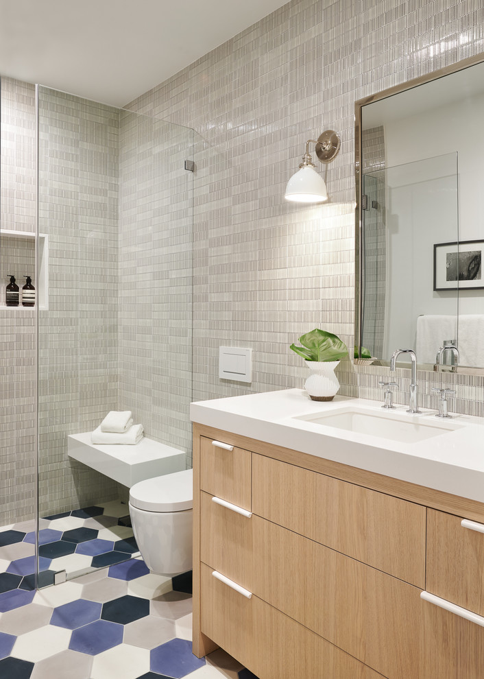 This is an example of a large transitional kids bathroom in San Francisco with flat-panel cabinets, light wood cabinets, a curbless shower, a wall-mount toilet, ceramic tile, cement tiles, an undermount sink, quartzite benchtops, blue floor, a hinged shower door, white benchtops and gray tile.