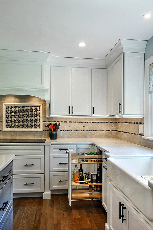 Photo of a transitional l-shaped eat-in kitchen in Philadelphia with a farmhouse sink, recessed-panel cabinets, white cabinets, quartz benchtops, grey splashback, subway tile splashback, black appliances, medium hardwood floors, with island, brown floor and white benchtop.