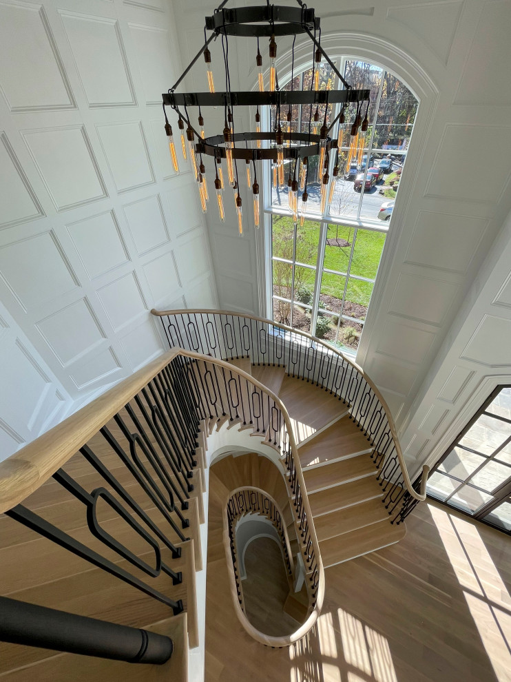 Expansive transitional wood curved staircase in DC Metro with wood risers, mixed railing and decorative wall panelling.