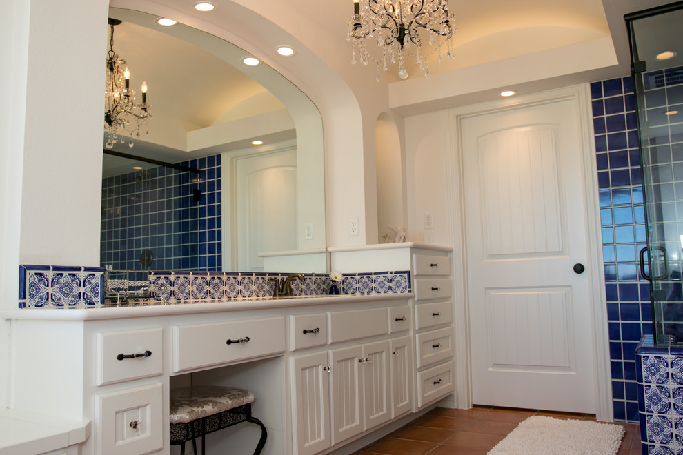 Large master bathroom in Austin with recessed-panel cabinets, white cabinets, a corner shower, a two-piece toilet, blue tile, ceramic tile, white walls, terra-cotta floors, an undermount sink, solid surface benchtops, orange floor, a hinged shower door and white benchtops.