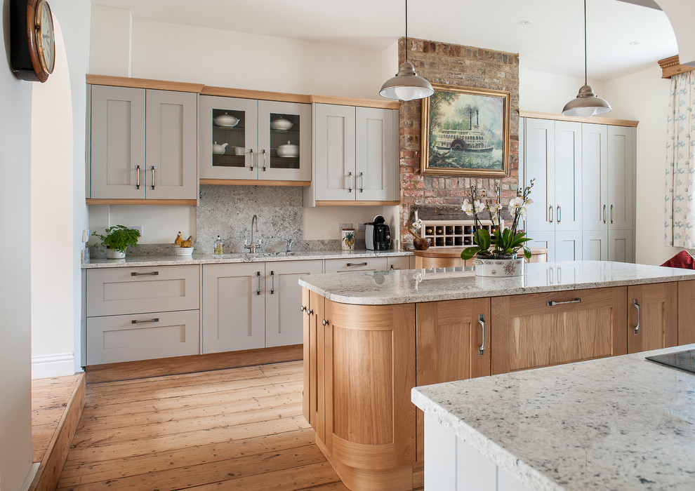 This is an example of a traditional kitchen in Kent with an undermount sink, shaker cabinets, grey cabinets, stone slab splashback, panelled appliances, light hardwood floors and with island.