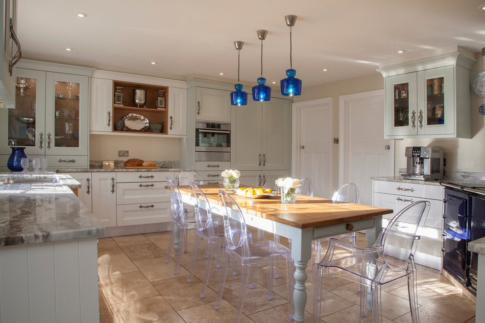 This is an example of a country l-shaped eat-in kitchen in Surrey with recessed-panel cabinets, blue cabinets, beige splashback, black appliances, travertine floors and no island.