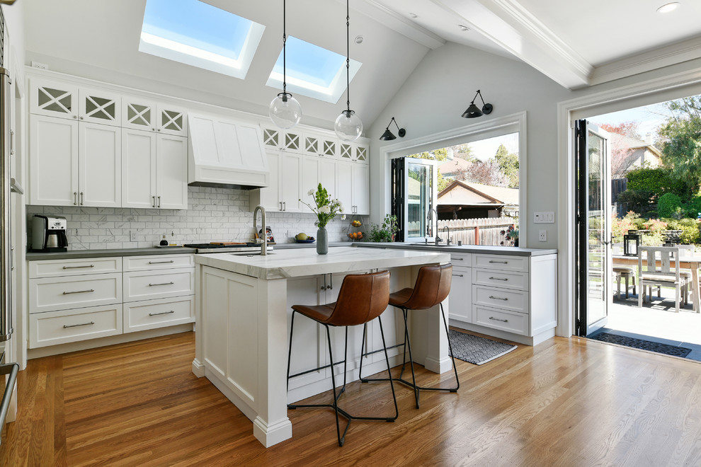 Mid-sized transitional u-shaped open plan kitchen in San Francisco with an undermount sink, shaker cabinets, white cabinets, white splashback, stainless steel appliances, medium hardwood floors, with island, brown floor, grey benchtop, concrete benchtops and marble splashback.