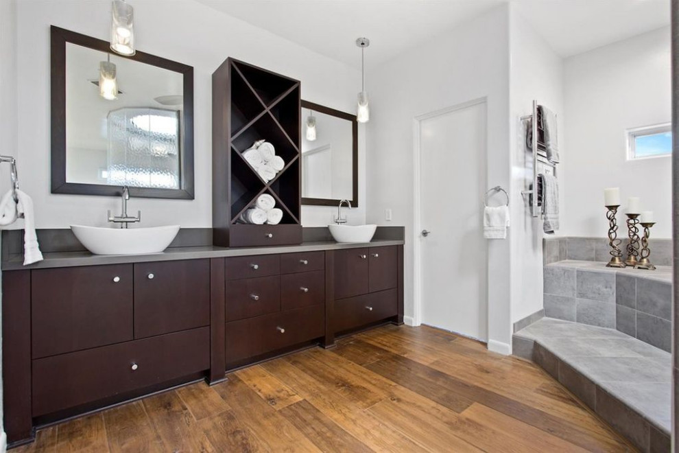 Expansive contemporary master bathroom in Sacramento with flat-panel cabinets, dark wood cabinets, a corner tub, an open shower, a one-piece toilet, gray tile, stone tile, white walls, medium hardwood floors, a vessel sink, zinc benchtops, brown floor, an open shower and grey benchtops.