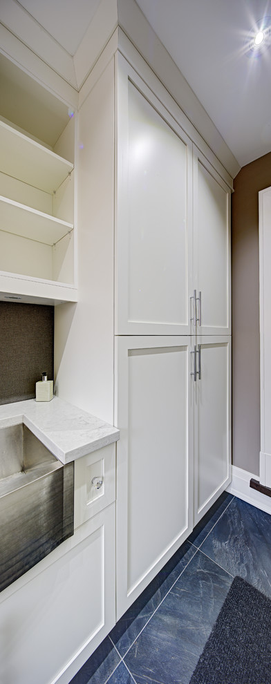 Photo of a small galley dedicated laundry room in Toronto with a farmhouse sink, shaker cabinets, white cabinets, quartz benchtops, grey walls and blue floor.