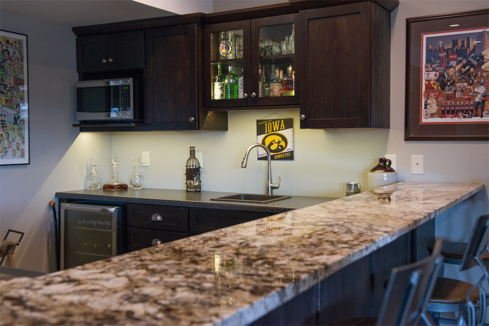 This is an example of a large arts and crafts l-shaped seated home bar in Cedar Rapids with shaker cabinets, dark wood cabinets, a drop-in sink, laminate benchtops and travertine floors.