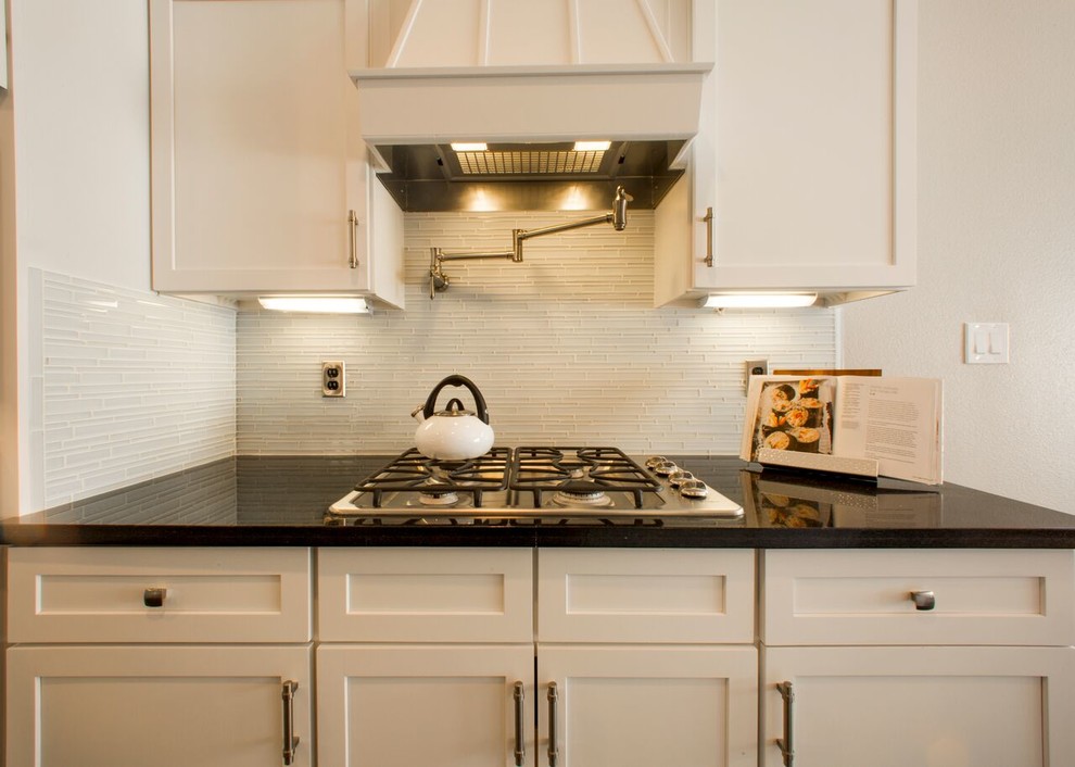 Example of a transitional porcelain tile eat-in kitchen design in Austin with an undermount sink, shaker cabinets, white cabinets, granite countertops, white backsplash, glass sheet backsplash, stainless steel appliances and an island