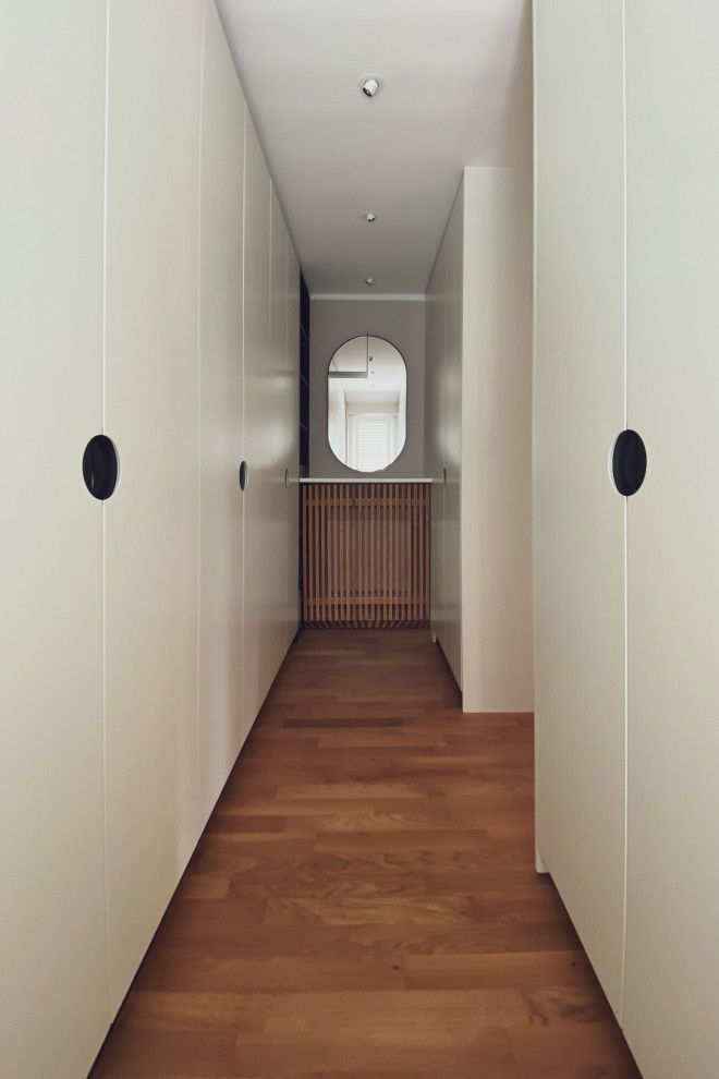 Cette photo montre un dressing et rangement tendance neutre avec un placard à porte plane, des portes de placard blanches, un sol en bois brun et un sol marron.