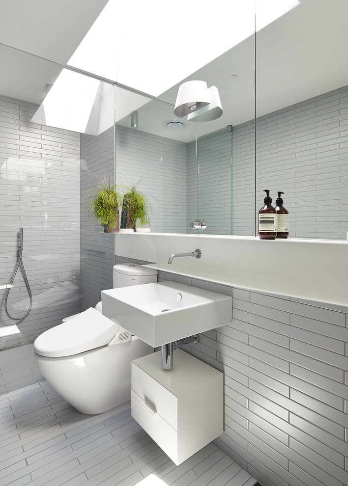 Photo of a contemporary bathroom in Melbourne with flat-panel cabinets, white cabinets, an alcove shower, a two-piece toilet, white tile and a wall-mount sink.