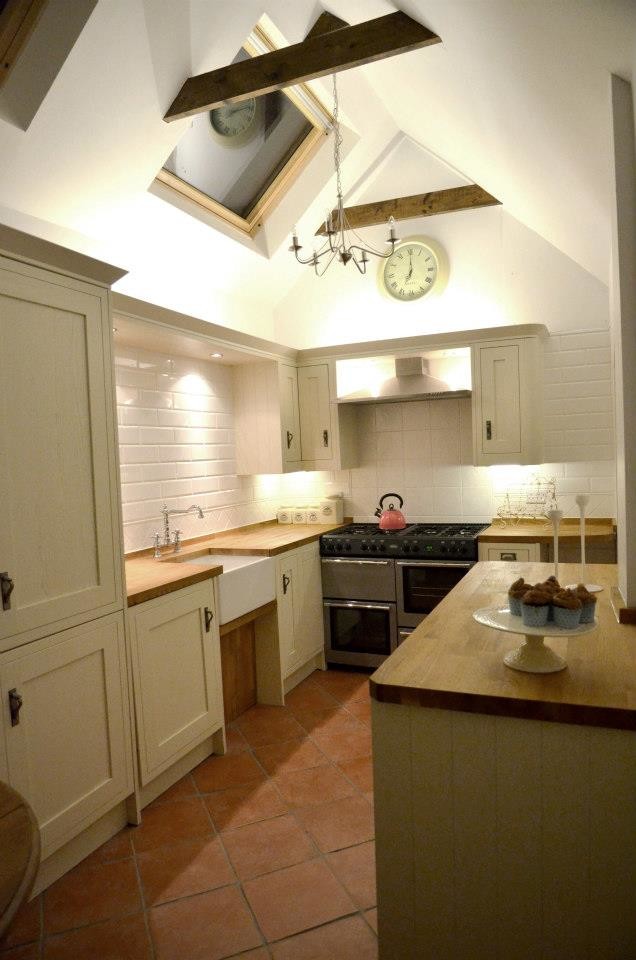 Photo of a small country galley separate kitchen in Other with a farmhouse sink, beige cabinets, wood benchtops, white splashback, porcelain splashback, stainless steel appliances, terra-cotta floors and no island.