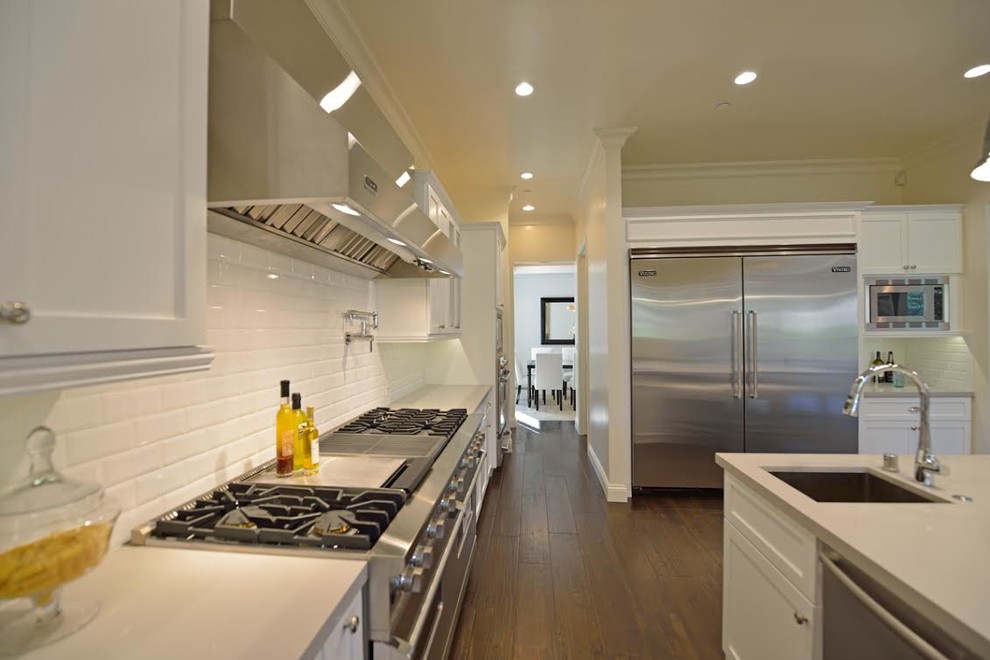 Large transitional u-shaped dark wood floor and brown floor eat-in kitchen photo in Los Angeles with an undermount sink, recessed-panel cabinets, white cabinets, granite countertops, white backsplash, ceramic backsplash, stainless steel appliances and an island
