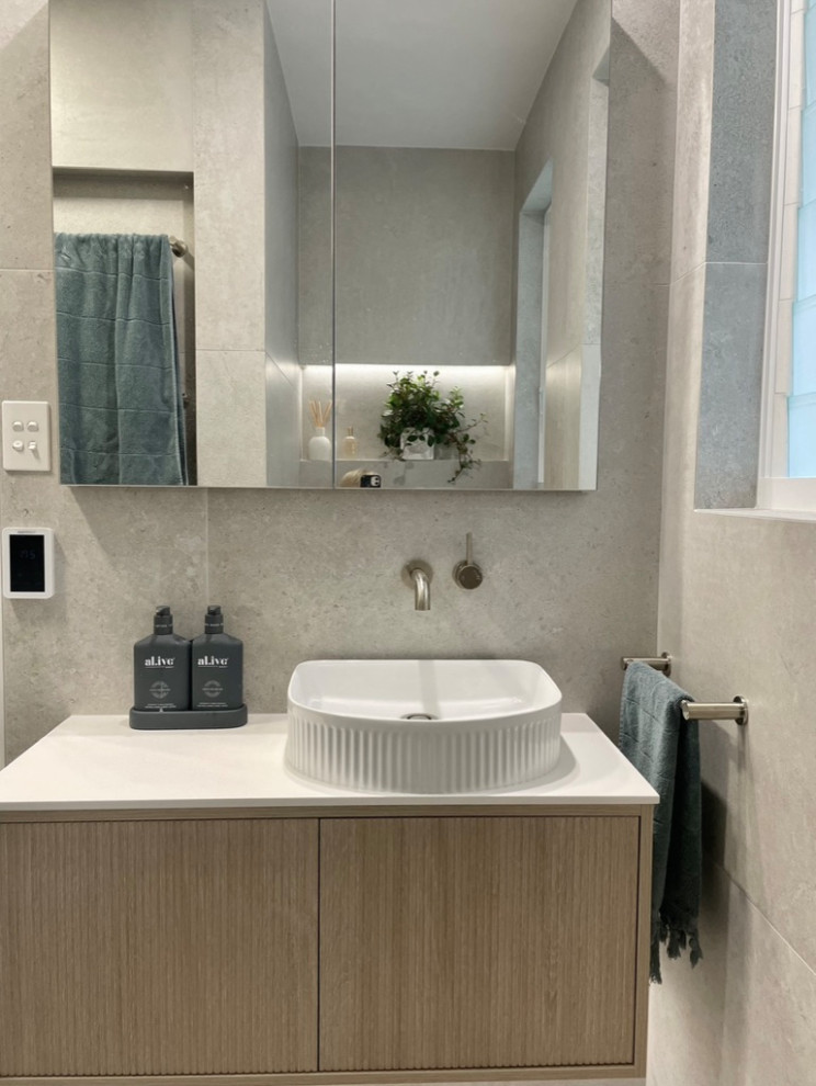На фото: маленькая ванная комната в современном стиле с фасадами островного типа, светлыми деревянными фасадами, душем в нише, унитазом-моноблоком, серой плиткой, керамической плиткой, серыми стенами, полом из керамической плитки, душевой кабиной, настольной раковиной, столешницей из искусственного камня, серым полом, душем с распашными дверями, белой столешницей, нишей, тумбой под одну раковину и подвесной тумбой для на участке и в саду с