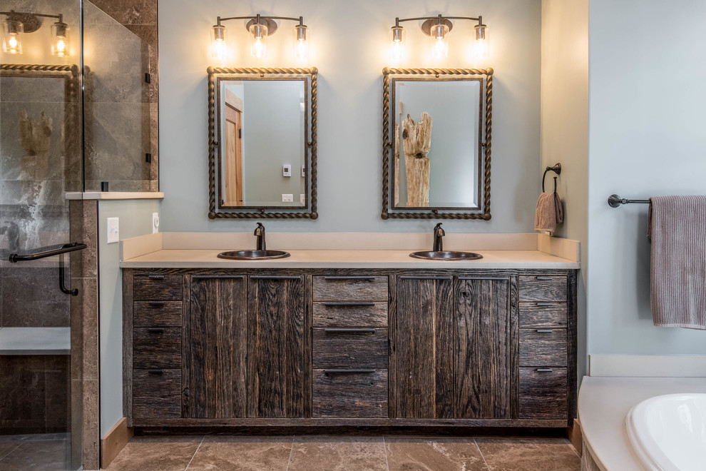 Example of a large mountain style master brown tile and stone slab brown floor drop-in bathtub design with flat-panel cabinets, dark wood cabinets, gray walls, a drop-in sink, solid surface countertops, a hinged shower door and gray countertops