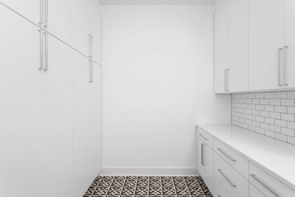 Exempel på en stor modern vita u-formad vitt tvättstuga enbart för tvätt, med en undermonterad diskho, släta luckor, vita skåp, marmorbänkskiva, vitt stänkskydd, stänkskydd i keramik, vita väggar, klinkergolv i keramik, en tvättmaskin och torktumlare bredvid varandra och flerfärgat golv