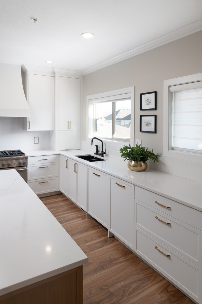 Large u-shaped medium tone wood floor kitchen photo with an undermount sink, shaker cabinets, white cabinets, quartzite countertops, white backsplash, an island and white countertops