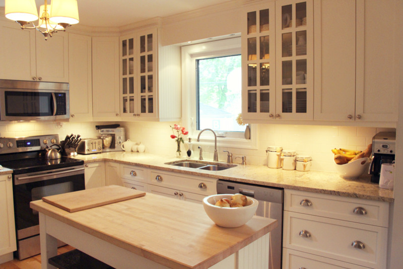 Example of a large transitional l-shaped light wood floor and beige floor kitchen design with white cabinets, granite countertops, stainless steel appliances, an island, a double-bowl sink, shaker cabinets, white backsplash and ceramic backsplash