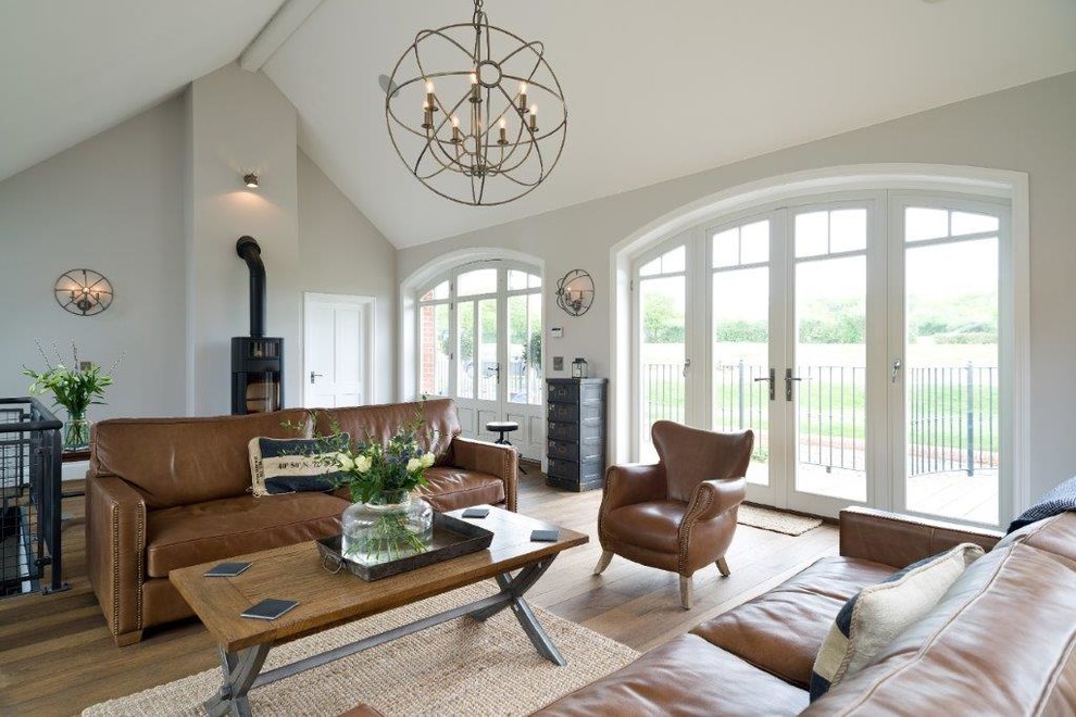 Photo of a large country open concept living room in Other with grey walls, light hardwood floors, a wood stove and beige floor.
