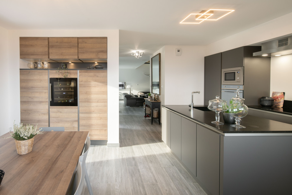 Large modern galley kitchen in Grenoble with grey cabinets, granite benchtops, black splashback, with island, black benchtop, granite splashback, stainless steel appliances and painted wood floors.