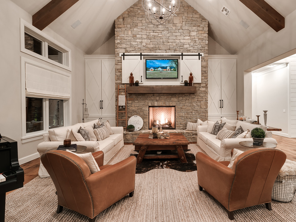 This is an example of a country open concept family room in Oklahoma City with beige walls, light hardwood floors, a standard fireplace, a stone fireplace surround, a wall-mounted tv and beige floor.