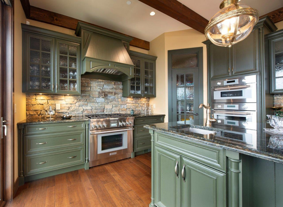 Design ideas for a large arts and crafts l-shaped open plan kitchen in Other with a farmhouse sink, glass-front cabinets, green cabinets, granite benchtops, limestone splashback, stainless steel appliances, medium hardwood floors, with island, brown floor and green benchtop.