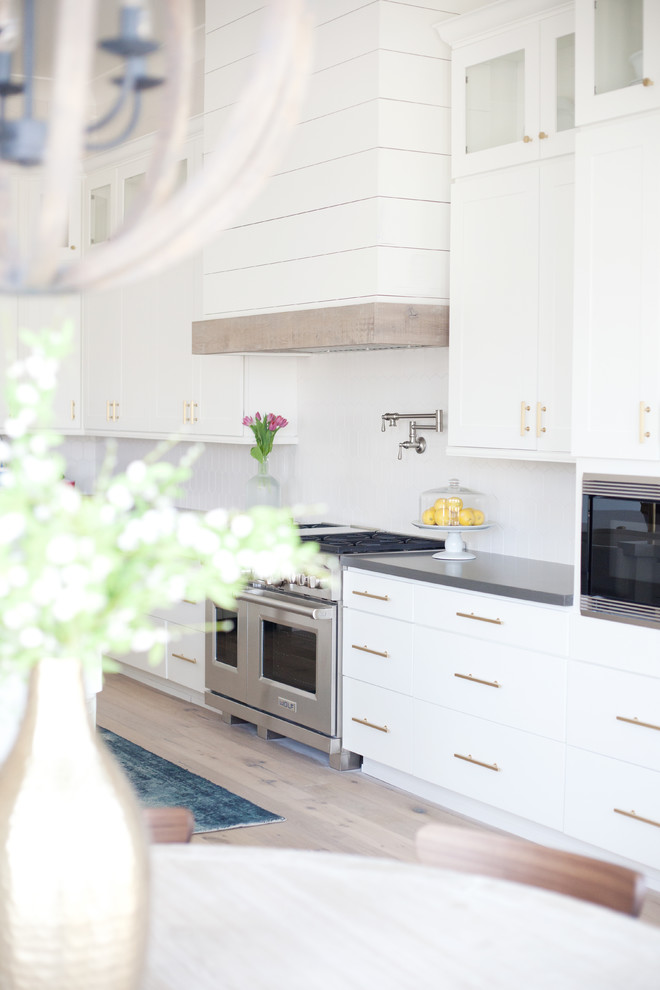 Inspiration for a large contemporary l-shaped light wood floor and gray floor eat-in kitchen remodel in Phoenix with a farmhouse sink, shaker cabinets, white cabinets, quartzite countertops, white backsplash, porcelain backsplash, stainless steel appliances and an island