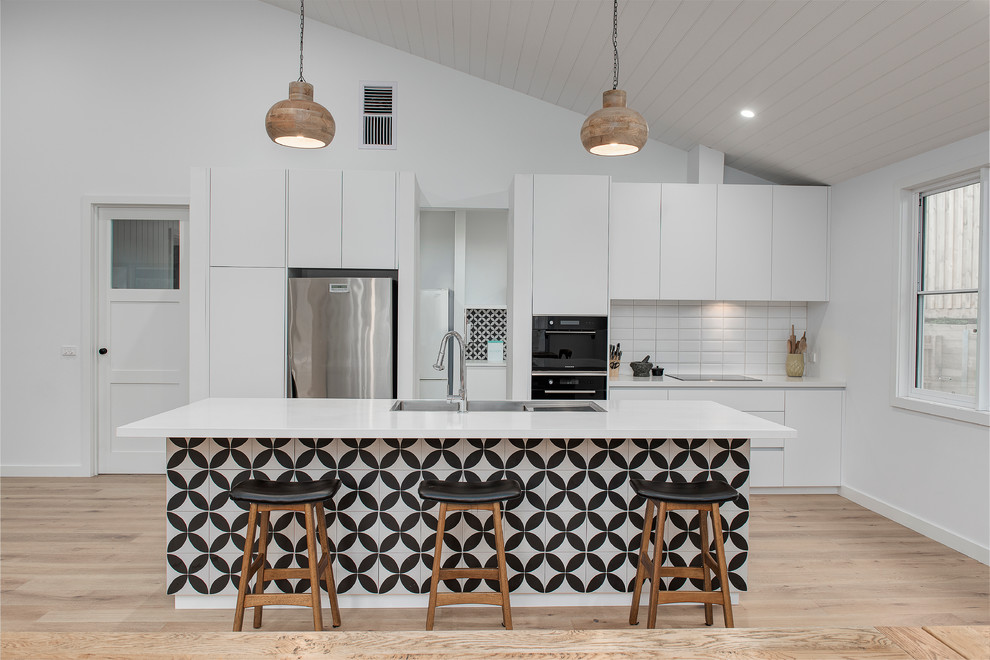 Inspiration for a contemporary galley kitchen in Melbourne with a drop-in sink, flat-panel cabinets, white cabinets, white splashback, stainless steel appliances, light hardwood floors and with island.