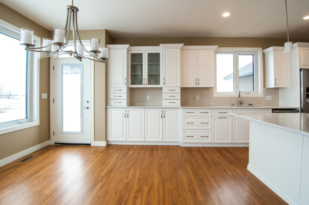Eat-in kitchen - huge transitional l-shaped vinyl floor and brown floor eat-in kitchen idea in Calgary with an undermount sink, raised-panel cabinets, white cabinets, quartz countertops, white backsplash, subway tile backsplash, stainless steel appliances and an island