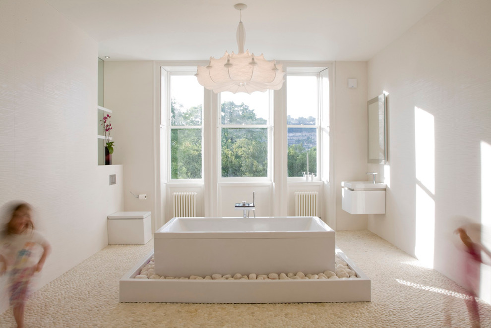 This is an example of a large modern master bathroom in Other with a wall-mount sink, flat-panel cabinets, white cabinets, a freestanding tub, an open shower, a one-piece toilet, white tile, ceramic tile, white walls and pebble tile floors.