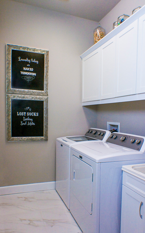 Photo of a small contemporary galley dedicated laundry room in Tampa with a single-bowl sink, shaker cabinets, white cabinets, solid surface benchtops, grey walls, porcelain floors and a side-by-side washer and dryer.