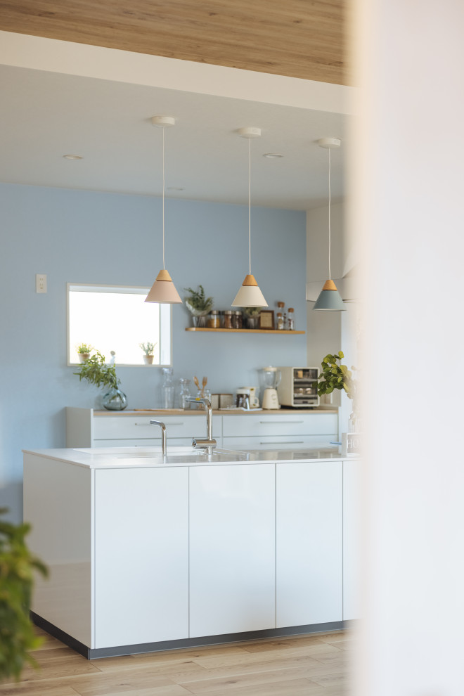 Photo of a mid-sized scandinavian single-wall open plan kitchen in Other with flat-panel cabinets, white cabinets, white splashback, light hardwood floors, beige floor, white benchtop and wallpaper.